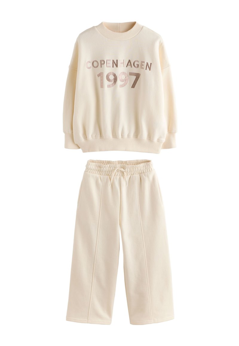 Sweat-shirt en polaire couleur crème avec imprimé "COPENHAGEN 1997", associé à un pantalon assorti à taille élastique, doté de poches latérales et de jambes larges.