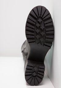 Suela de bota de goma negra con profundas ranuras de tracción y patrones elevados. Material superior liso con detalle de cremallera lateral.