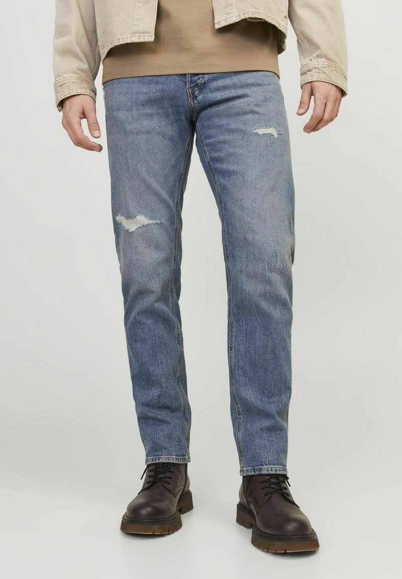 Vaqueros de mezclilla azul claro con corte recto, que presentan detalles desgastados y un lavado medio. Combinados con botas de cuero marrón oscuro con cordones.