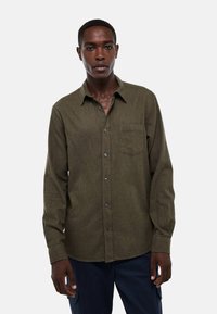 Chemise olive verte à manches longues avec un poche poitrine, des boutons à l'avant et une texture subtile. Convient pour une tenue décontractée.