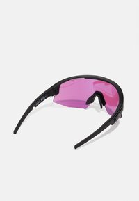 Lunettes de soleil avec une monture en plastique noir, au design incurvé et aux verres teintés rose. Elles présentent des branches flexibles et un style minimaliste.