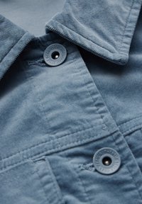 Chemise en velours côtelé bleu dotée d'un col classique, de boutons en plastique et d'un tissu texturé avec des coutures visibles et un détail de poche à patte.