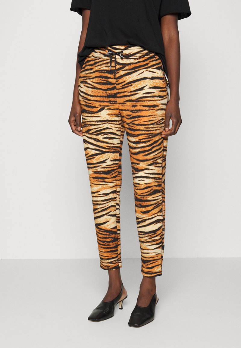 Olifantprint broek in oranje, zwart en beige. Gemaakt van lichtgewicht stof met een koord in de taille en een tapered fit. Effen zwarte top en schoenen.