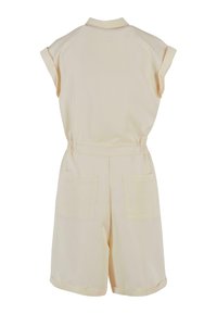 Combinaison beige à manches courtes avec poignets roulés, taille élastique, encolure avec col et deux poches plaquées au dos.