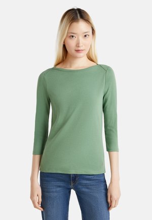 Grünes Langarmshirt mit Bootsausschnitt und Dreiviertelärmeln, aus glattem Stoff, kombiniert mit blauen Jeans.