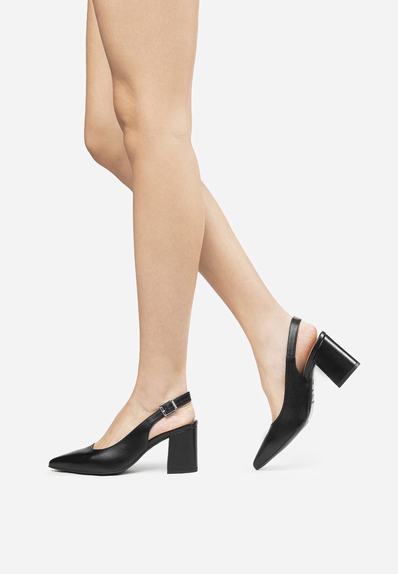 Des escarpins noirs à bride arrière avec un bout pointu, un talon épais et une sangle de cheville réglable ; texture en cuir lisse avec un design minimaliste.