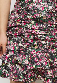 Mini mekko, jossa on musta pohja ja kukkakuosi, jossa on vaaleanpunaisia, valkoisia ja vihreitä kukkia. Rypytetty helma ja nyöritysrakenne lisäävät ulottuvuutta.