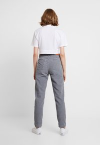 Avkortad vit t-shirt och ljusgrå ribbade byxor med sidofickor och synliga sömmar, ihop med vita sneakers mot en enfärgad bakgrund.