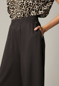 Zwarte wijde broek met een elastische tailleband en zijzakken. De stof heeft een gladde textuur en een lichte glans.