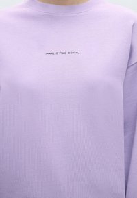 Ανοιχτό μωβ φούτερ με στρογγυλή λαιμόκοψη και το κείμενο "MARC O'POLO DENIM" τυπωμένο με μικρά μαύρα γράμματα στο κέντρο του στήθους.