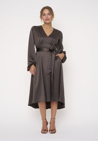 Braunes Satin-Kleid mit V-Ausschnitt, langen Ärmeln und Taillengürtel. Mit gerafften Manschetten und einem asymmetrischen Saumdesign.
