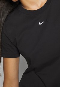 Černé bavlněné tričko s kulatým výstřihem a krátkými rukávy, které má na horní levé části hrudi malé bílé logo Nike.