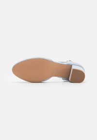 Blue suede high-heeled shoe with a textured light brown sole and rounded toe. Features a chunky heel and minimal hardware detail.