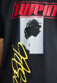 Black cotton t-shirt featuring bold red and yellow text, a graphic of a profile in white, and blue accents.