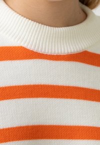 Gestreifter Pullover mit weißer Basis und kräftigen, orangefarbenen horizontalen Streifen. Verfügt über einen gerippten Ausschnitt und weichen, strukturierten Stoff.