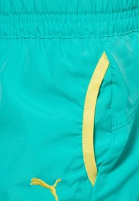 Tyrkysové sportovní šortky z lehké látky, s žlutými akcenty na kapsách a malým žlutým logem, s elastickým pasem.