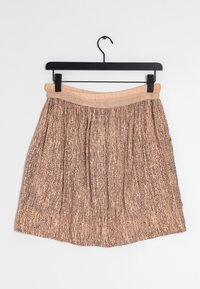 Záhybová sukně z měkké broskvové látky s hnědým abstraktním vzorem, s elastickým pasem a střední délkou, zavěšená na černém ramínku.