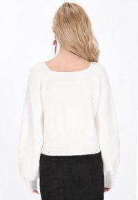 Pull en maille blanche avec un col arrière carré, des poignets côtelés et une coupe ample. Le pull présente des détails texturés et une finition douce.