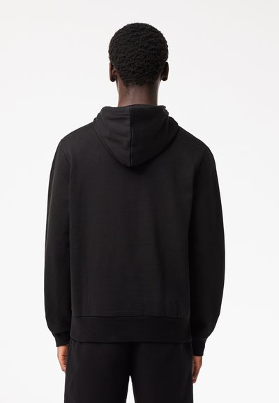 Hoodie noir en tissu doux, doté d'une capuche et de manches longues. Le design comprend des poignets côtelés et une coupe décontractée pour plus de confort.