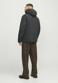Zwarte gewatteerde jas met capuchon, met een rechte snit en zachte textuur, gecombineerd met bruine wijde broek en zwarte schoenen.