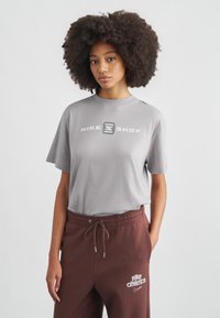 Šedé bavlnené tričko s krátkymi rukávmi, na prednej strane s bielym logom "NIKE SHOX"; doplnené voľnými hnedými teplákmi s detailom loga.