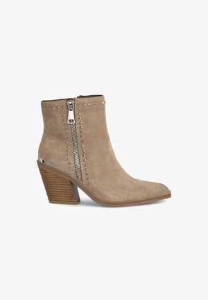 Beige Wildleder-Ankle-Boot mit spitzem Zehenbereich, einem dekorativen seitlichen Reißverschluss, silbernen Nieten und einem Blockabsatz aus Holz.