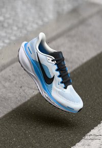 Nike futócipő, légáteresztő fehér hálós felsőrésszel, kék részletekkel, fekete pipa logóval és párnázott talppal a kényelem érdekében.