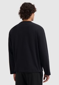 Black long-sleeve shirt, soft cotton fabric, relaxed fit, round neckline, minimal stitching detail on the back, no visible patterns or accents.