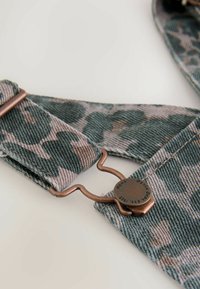 Green and beige camo-patterned denim suspenders with copper hardware and a clip closure, featuring textured fabric and stitched edges.