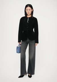 Μαύρο ριγωτό πουλόβερ με κουμπιά και στρογγυλή βάση, σε συνδυασμό με γκρίζα τζιν ψηλής μέσης. Κρατώντας μια μικρή μπλε τσάντα και φοράει μαύρα τακούνια.