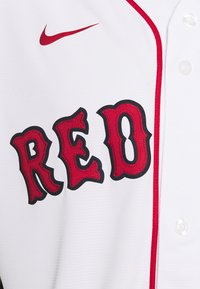 Biała koszulka baseballowa z czerwonym napisem "RED" w czarnym obrysie, logo Nike w kolorze czerwonym oraz białymi guzikami na plisie.