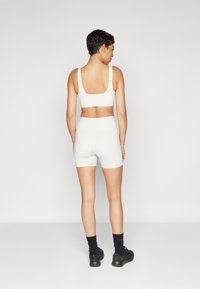 Reggiseno sportivo bianco senza cuciture e pantaloni corti a vita alta, design aderente, texture morbida, superficie liscia, abbinato a sneaker e calze scure.
