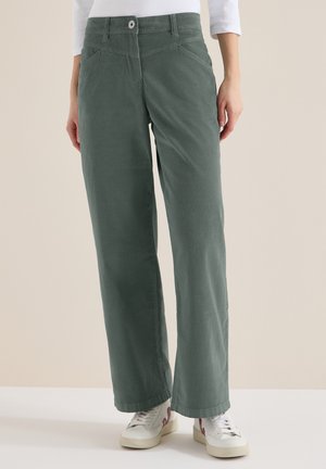 Pantalon vert à jambes larges avec poches avant et fermeture à boutons, porté avec des baskets blanches et un haut blanc à manches longues.
