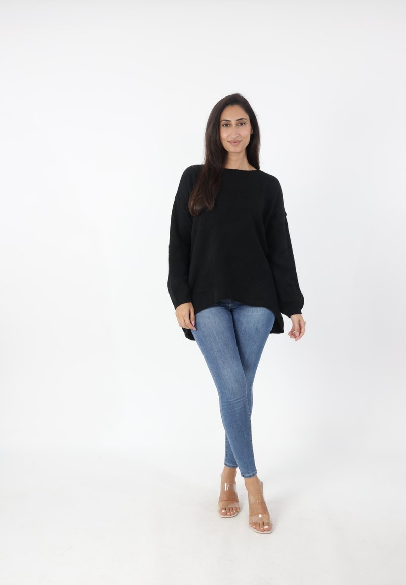 Zwarte oversized trui met lange mouwen, gecombineerd met lichtblauwe aangesloten jeans en doorzichtige blokhak sandalen. Eenvoudig en minimalistisch ontwerp.
