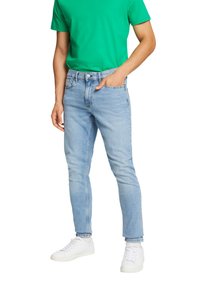 Jeans din denim albastru deschis, cu croială slim, design cu cinci buzunare și bucle pentru curea, asortați cu un tricou verde cu guler rotund și teniși albi.