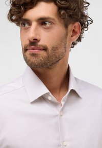 Camicia a trama lilla chiara con colletto a punta e chiusura a bottoni, caratterizzata da motivi sottili; il tessuto sembra liscio e aderente.
