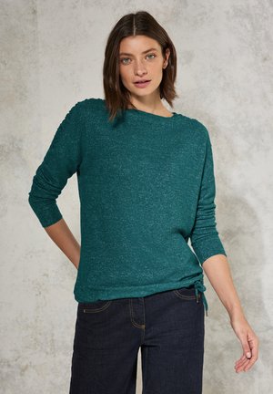 Teal lange mouwen top gemaakt van zachte stof. Heeft een ronde halslijn, zijstrikdetails en geribbelde accenten op de schouders. Gekozen in combinatie met donkere jeans.