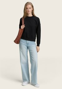 Felpa nera con texture a costine, jeans larghi blu chiaro e sneaker bianche. Borsa a tracolla in pelle marrone. 