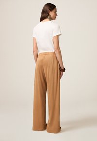 T-shirt blanc à manches courtes associé à un pantalon large beige avec une taille élastique. Texture douce et coupe décontractée.