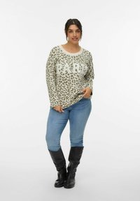 Khaki luipaardprinttrui met "PARIS" in witte letters, ontspannen pasvorm, ronde halslijn, gecombineerd met blauwe jeans en zwarte kniehoge laarzen.