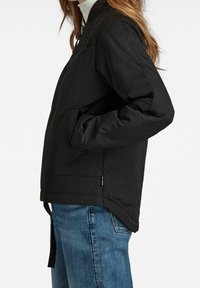 Czarna kurtka bomberka z zamkiem z przodu, bocznymi kieszeniami i ściągaczami na rękawach. Posiada gładką, wyściełaną fakturę. W połączeniu z niebieskimi dżinsami.