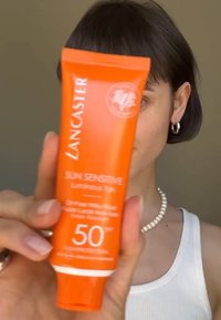 Lancaster Aurinkosuoja Luminous Tan -voide kirkkaassa oranssissa putkilossa, 50 SPF, jossa on valkoista tekstiä ja pyöreä logo. Sileä, muovinen pakkaus.