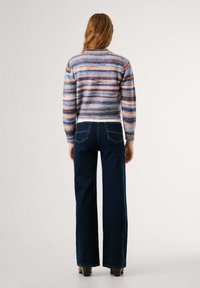 Multifarvet stribet sweater i blå, pink og creme med en rund halsudskæring, parret med mørkeblå brede jeans og hæle.