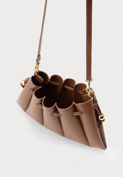 Καφέ δερμάτινη τσάντα χειρός με κυματιστές πλευρές, χρυσά μεταλλικά στοιχεία και μακρύ ρυθμιζόμενο ιμάντα ώμου σε λευκό φόντο.