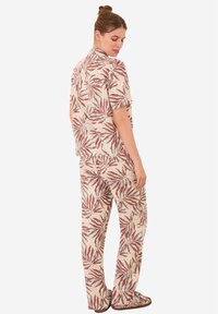 Korte mouwen overhemd en broek set in crème met een bladpatroon in rood en blauw. De stof lijkt lichtgewicht met een ontspannen pasvorm.