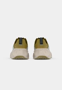 Sneakers Nike w szaro-oliwkowej cholewce, z teksturowanym piętkiem i wyściełaną beżową podeszwą. Posiadają czarną pętelkę z białymi kropkami.