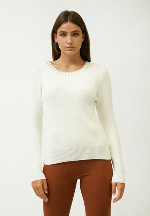 White ribbed sweater with long sleeves and a round neckline adorned with metallic bead accents around the collar. Soft texture, fitted design.