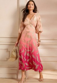 Maxi jurk in ombre tinten van roze met gouden veerpatronen, V-halslijn, pofmouwen en een vloeiende A-lijn silhouet. Gouden accessoires.