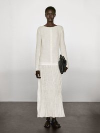 Langes, cremefarbenes Leinenkleid mit gerader Silhouette, rundem Ausschnitt und Knopfleiste. Kombiniert mit einer schwarzen geflochtenen Handtasche und gemusterten Sandalen.