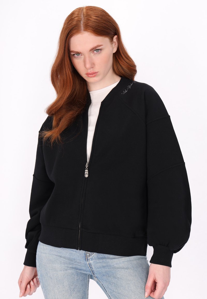Černá bomber bunda na zip s volným střihem, žebrovanými manžetami a lemem. Disponuje hladkým povrchem a jemným logem na rameni.